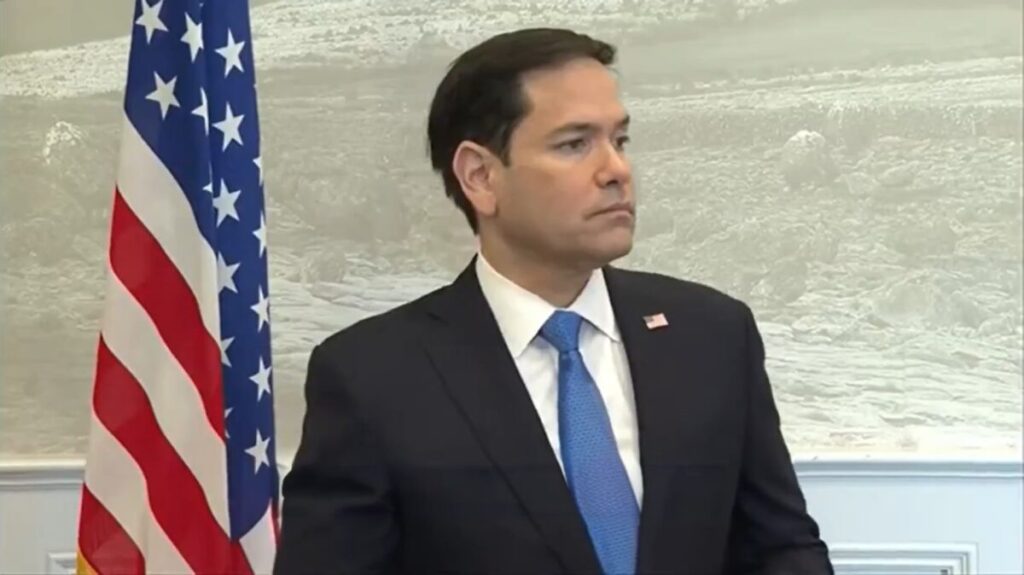 Marco Rubio standing near American flag looking to his left