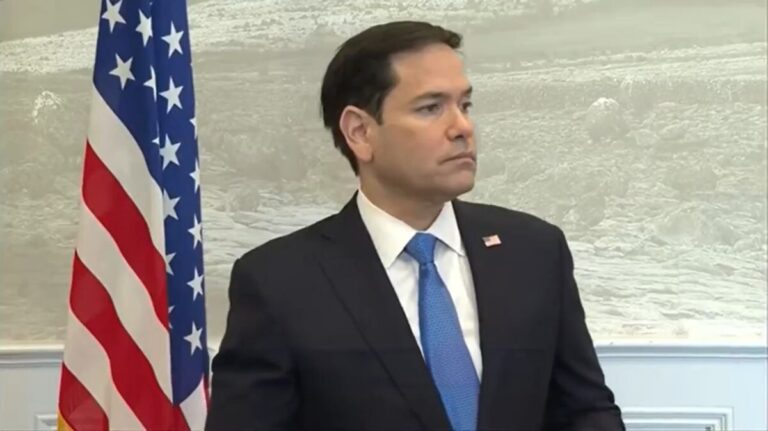 Marco Rubio standing near American flag looking to his left